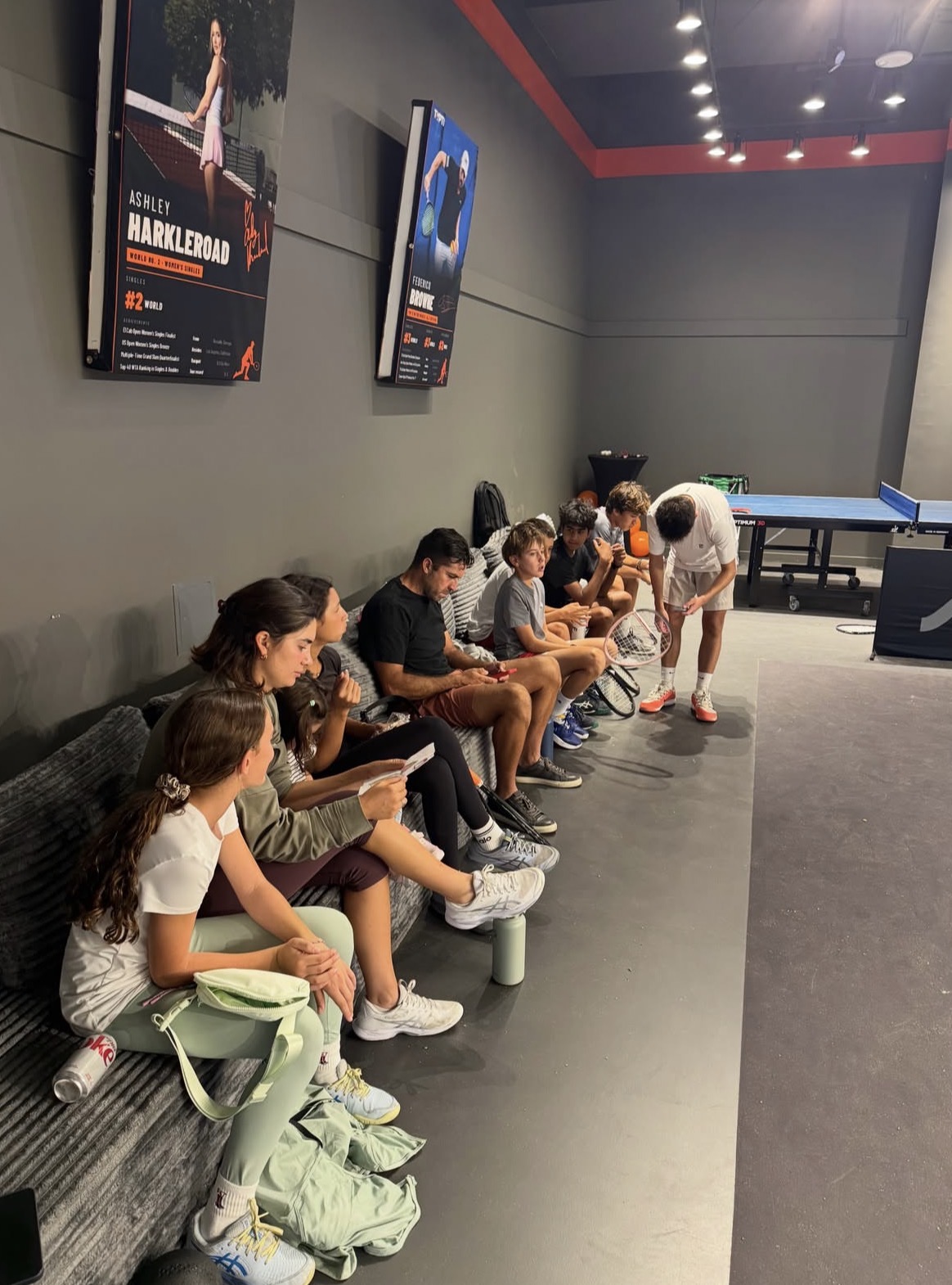 Kids and families seated along the couch at the Typti venue while a player warms up with a racket